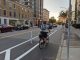 A person riding a bike in a curbside bike lane, separate from the general traffic lane by a painted buffer and plastic flexpost.