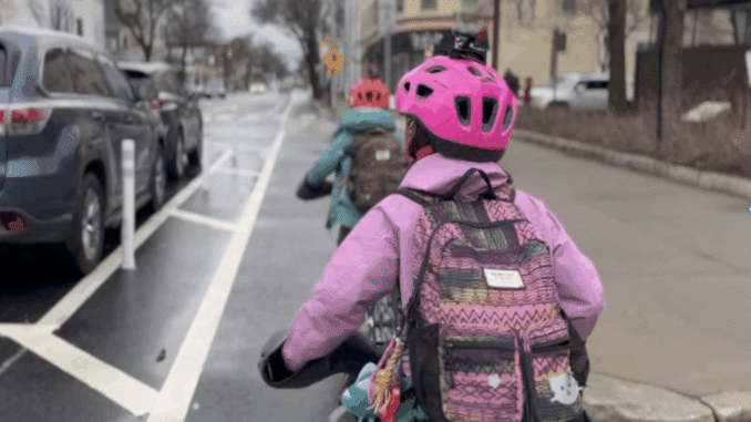 Two children in a bike lane - one in a pink jacket and helmet.