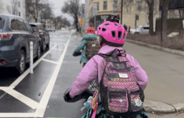Two children in a bike lane - one in a pink jacket and helmet.